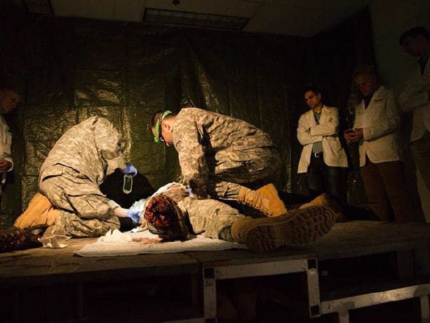 Clinicians observe a simulated combat rescue of a soldier who has lost part of a leg.