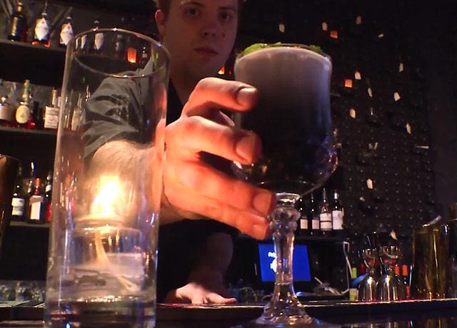 A bartender holds a drink made with charcoal