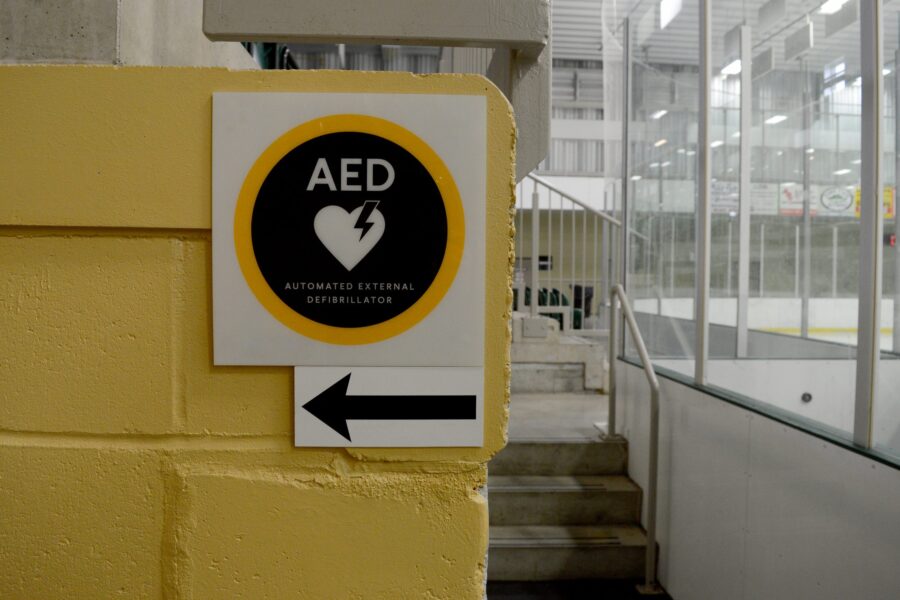 A sign directing emergency AED use inside a hockey arena.