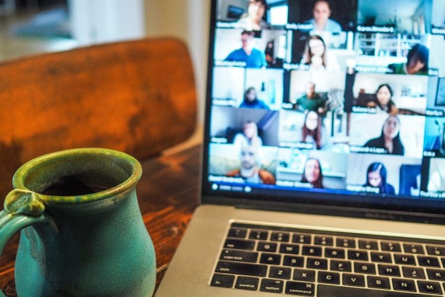 An open laptop with a Zoom meeting sitting next to a blue coffee mug.