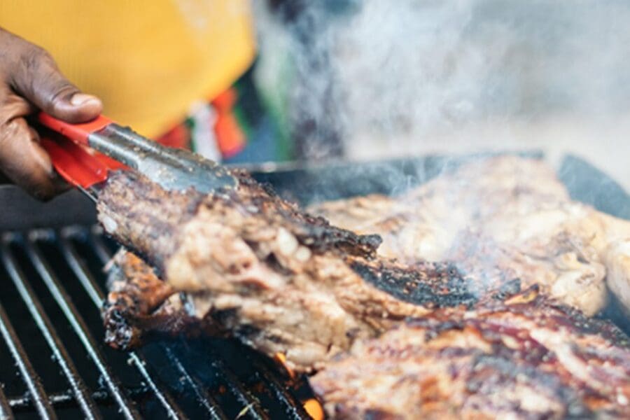 A Black man's hand flipping meat on a grill