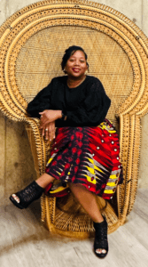 Woman wearing a black sweater and red and yellow skirt sitting in a throne-like chair