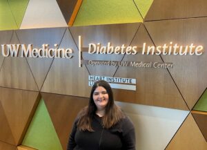 Woman with long brown hair wearing black shirt in front of a sign reading UW Medicine Diabetes Institute