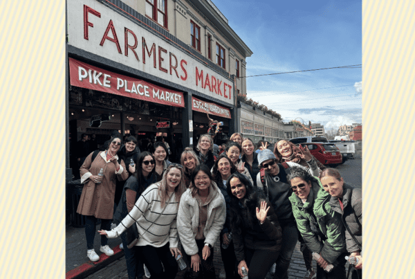 17 women smiling at Pike Place Market under a blue sky